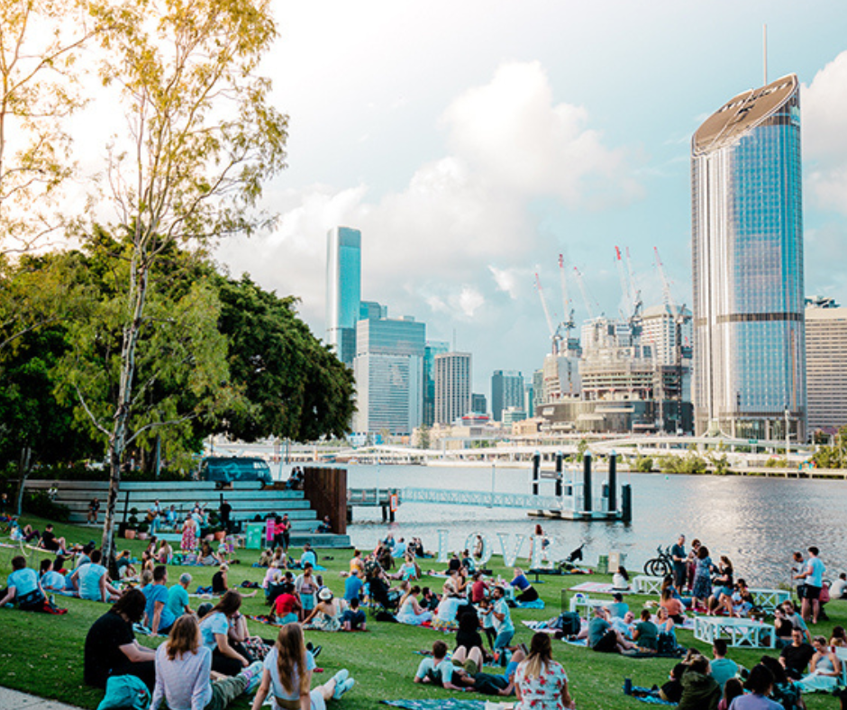 People sitting on the grass by the river enjoying a picnic.